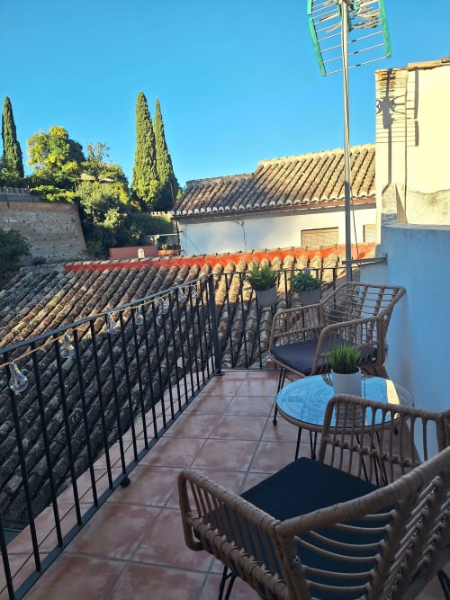 Soleada terraza en la azotea de Urban Suites Granada con sillas de mimbre, vistas a la ciudad y techos de azulejos históricos