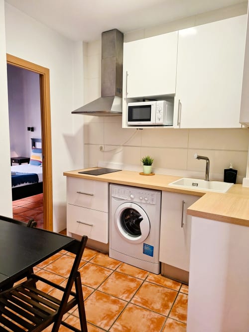 Cocina moderna con lavadora, encimera de madera y armarios rosa en apartamento Urban Suites Granada