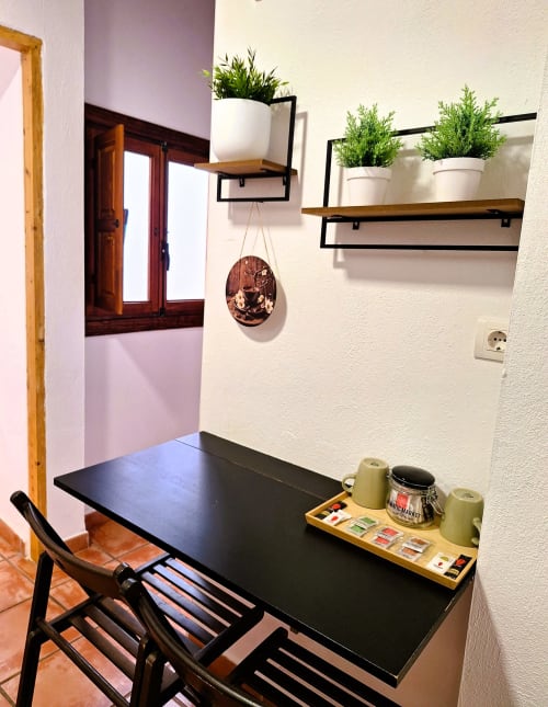 Espacio de trabajo moderno en Urban Suites Granada con escritorio negro, silla negra, estantes de madera con plantas en macetas y estación de café
