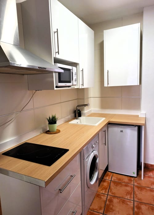 Cocina moderna en apartamento Urban Suites Granada con encimeras de madera, armarios blancos, placa de inducción y microondas