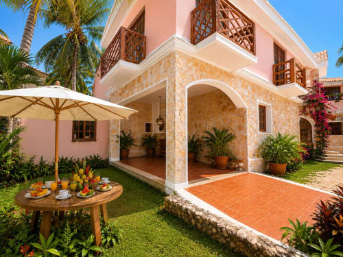 Isla Mujeres villa with pink hacienda architecture, stone archway, terracotta patio, garden seating, palm trees and flowering