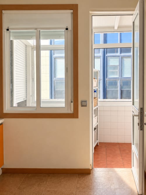 Cocina moderna en Baiona con muebles blancos, suelo de barro y gran ventanal con vistas a la ciudad