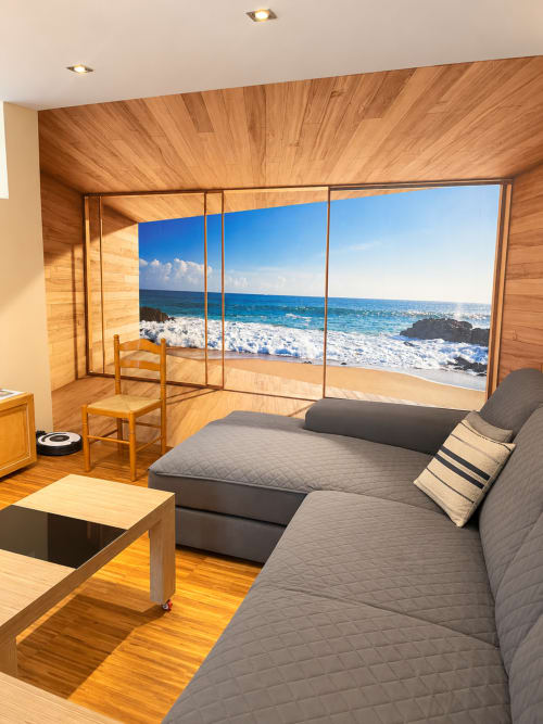 Dormitorio moderno con cama gris, suelos de madera y vistas al océano desde los grandes ventanales del apartamento Aire de Baiona en España