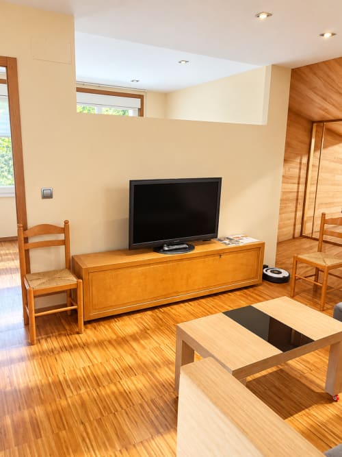 Luminoso salón del apartamento de Baiona con mueble TV de madera, televisor de pantalla plana, pisos de parqué y mobiliario rústico