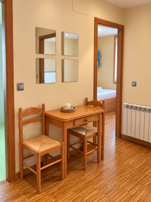 Acogedor comedor en apartamento de Baiona con mesa de madera, sillas, espejos y acceso al dormitorio por puerta de cristal