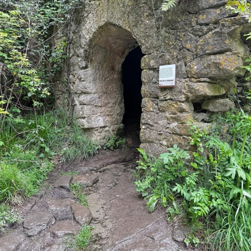 Entrada de arc de pedra de l'Hostal Collsacabra a L'Esquirol amb vegetació luxuriant i placa informativa