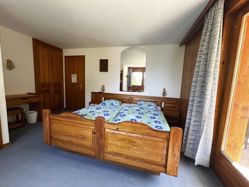 Chambre triple en bois à l'Hôtel les Bouquetins à Zinal, avec literie florale bleue et mobilier alpin