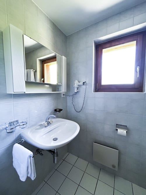 Salle de bains moderne de la Chambre Triple à l'Hôtel les Bouquetins Zinal avec lavabo blanc, miroir intégré et carrelage
