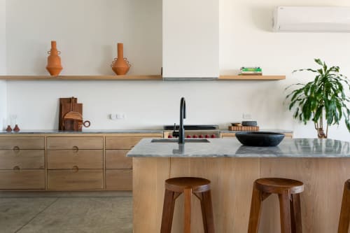 Modern kitchen at Casa Copal, Isla Mujeres resort with wooden cabinetry, stone countertop, black sink, and bar seating