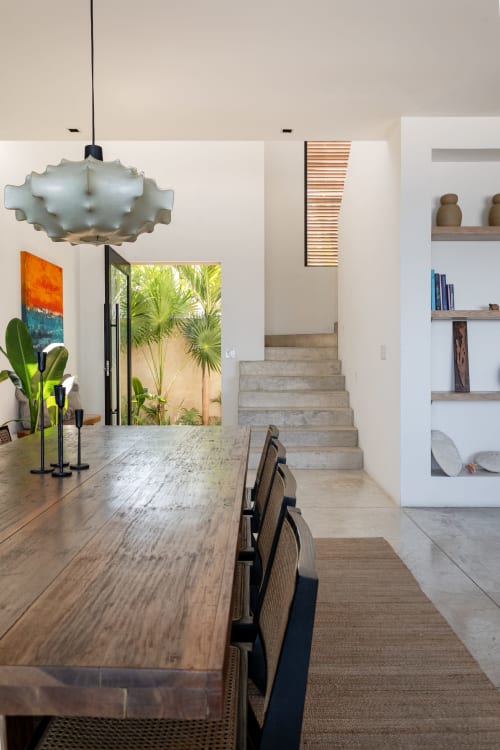 Modern dining room in Casa Copal cottage with wooden table, pendant light, tropical plants, and stairs to upper level in Isla