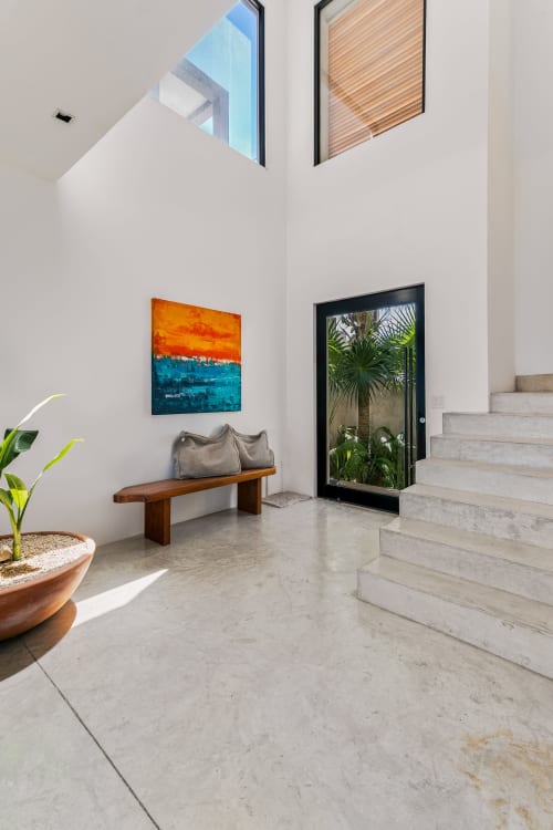 Modern coastal entryway at Casa Copal, Isla Mujeres with terrazzo floors, wooden bench, colorful artwork, and palm garden