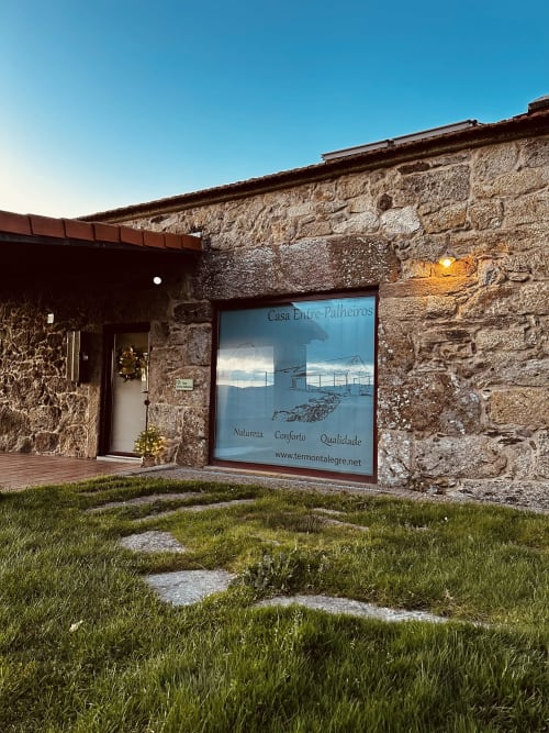 Casa Entre-Palheiros cottage exterior with stone walls, entrance door, and signage displaying nature, comfort, quality in