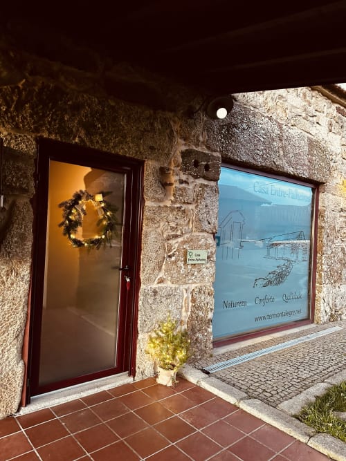 Casa Entre-Palheiros cottage entrance in Montalegre with decorated door, stone facade, and mountain view window display