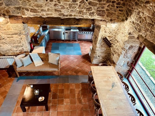 Overhead view of Casa Entre Palheiros cottage showing terracotta floors, stone walls, equipped kitchen, seating area, and