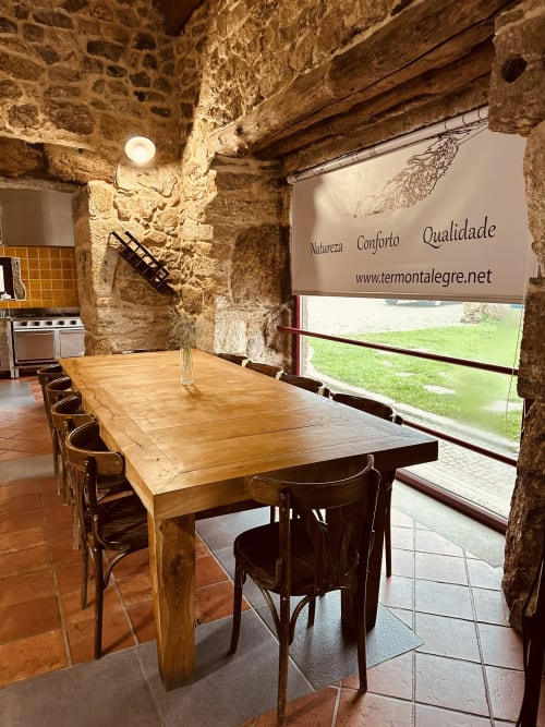 Rustic dining room with wooden table and chairs at Aconchego Rural cottage, stone walls, mountain view through window