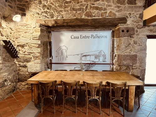 Rustic stone dining room at Casa Entre-Palheiros with wooden table and chairs, featuring exposed beams and property signage.