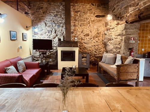 Rustic cottage living room with stone walls, fireplace, red sofa, and wooden furnishings at Aconchego Rural, Montalegre