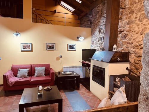 Cozy living room at Aconchego Rural cottage in Montalegre with red sofa, fireplace, TV, and rustic stone walls