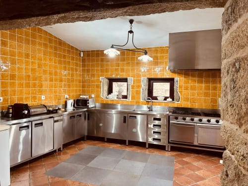 Spacious kitchen at Aconchego Rural cottage with orange tiles, stainless steel appliances, and rustic stone walls in