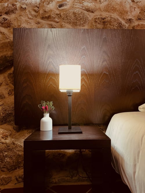 Bedroom nightstand with illuminated lamp and white flower vase at Aconchego Rural cottage, rustic stone walls backdrop