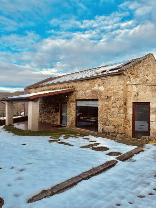 Stone cottage at Aconchego Rural with snow-covered ground, red doors, and mountain views under blue sky