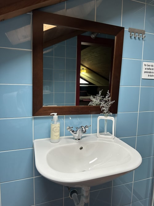 Modern bathroom sink with dark wood mirror and light blue tile walls at Aconchego Rural cottage in Montalegre, Portugal