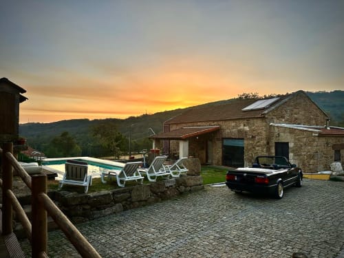 Sunset at Aconchego Rural cottage with pool, lounge chairs, and black convertible overlooking Montalegre mountains