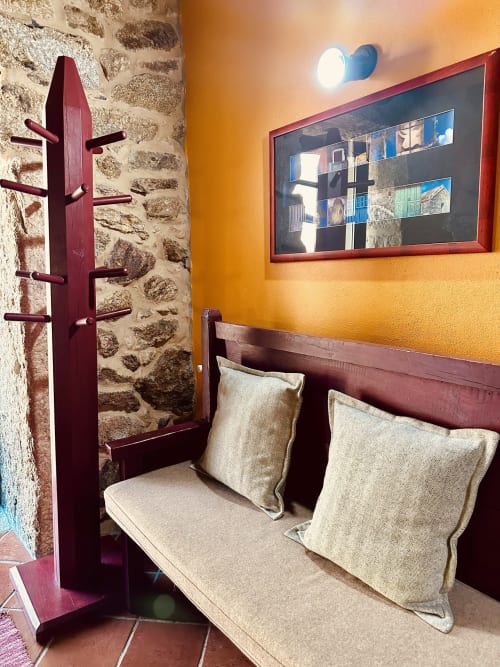 Cozy sitting nook in Casa Entre Palheiros cottage with beige cushioned bench, burgundy wooden coat stand, stone wall, orange
