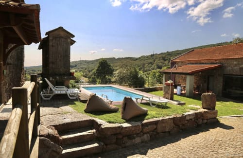 Mountain cottage pool area with loungers, stone terrace, and rustic buildings overlooking forested hills at Aconchego Rural,