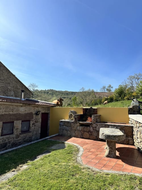 Stone cottage exterior with terracotta patio, yellow accent wall, and mountain views in Montalegre, Portugal