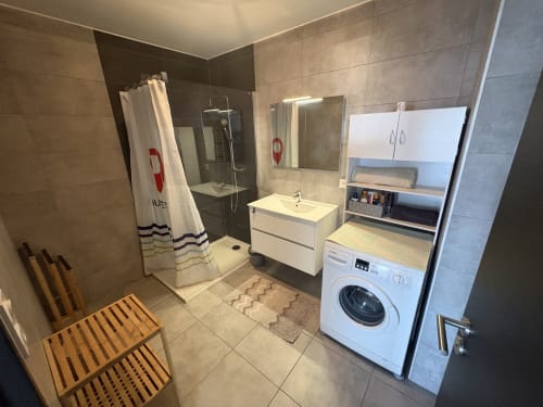 Salle de bain moderne avec douche, lavabo, machine à laver et rangements blancs à l'appartement Conciergerie De Porticcio