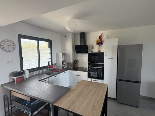 Cuisine moderne à l'appartement de Porticcio avec électroménagers noirs, meubles blancs, îlot central et vue sur la mer
