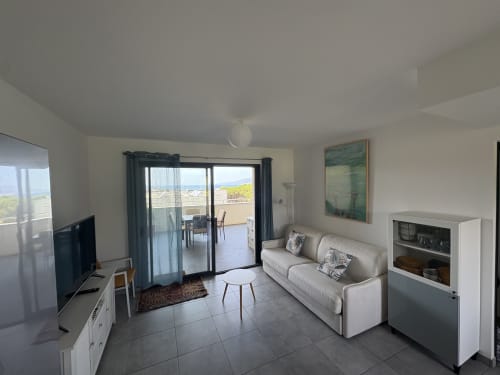 Salon moderne à la Conciergerie De Porticcio avec canapé beige, TV et vue sur la mer par les portes vitrées