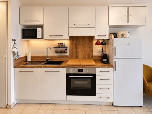 Cuisine compacte et moderne avec armoires blanches, plan de travail en bois, four noir et réfrigérateur blanc dans l'appartement de L'Île-Rousse