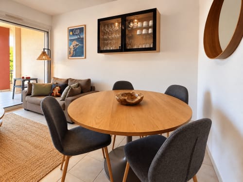 Salle à manger moderne avec table ronde en bois et chaises anthracite, salon avec canapé, vitrine et accès à la terrasse