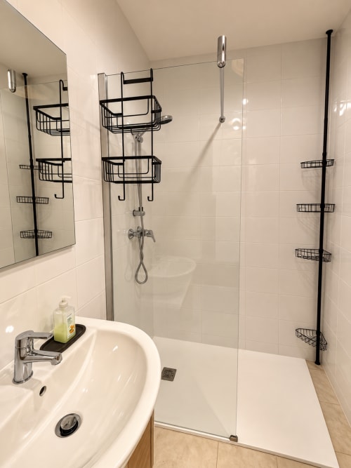 Douche moderne avec porte vitrée, carrelage blanc, paniers de rangement en métal noir dans l'appartement de L'Île-Rousse