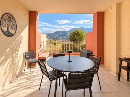 Terrasse ensoleillée avec table ronde face aux montagnes de Calvi, appartement à L'Île-Rousse avec vue sur la ville