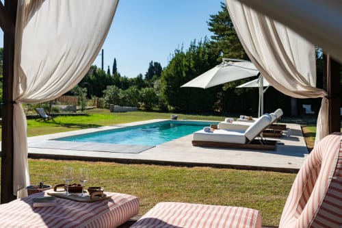 Terrasse luxueuse au bord de la piscine de Domaine Mas Lafleur avec transats, parasol et rideaux suspendus surplombant Châteaurenard