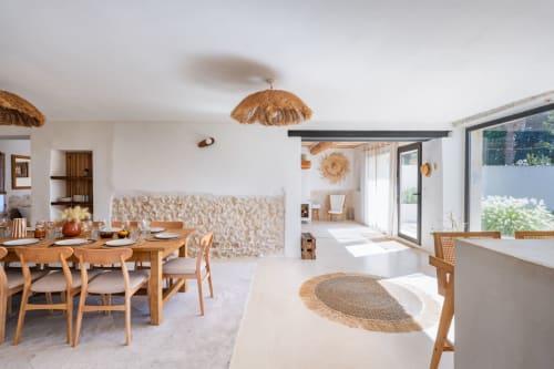 Salle à manger lumineuse du Domaine Mas Lafleur avec table en bois, lustres en osier, mur en pierre et vue sur le jardin