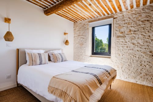 Chambre lumineuse au Domaine Mas Lafleur à Châteaurenard avec poutres apparentes, murs en pierre, lit queen-size et fenêtre à cadre noir