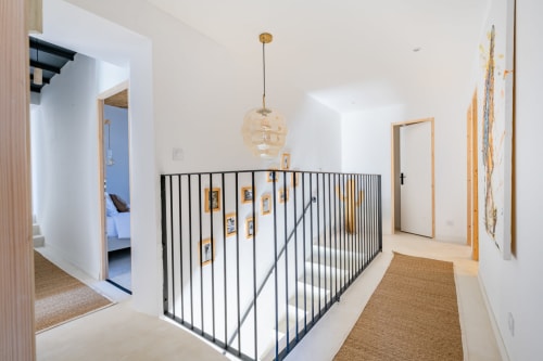 Couloir de mezzanine contemporain au Domaine Mas Lafleur avec rampe en métal noir, luminaire suspendu et œuvres encadrées