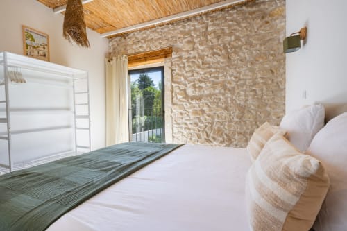 Chambre lumineuse au Domaine Mas Lafleur avec mur en pierre, literie blanche et porte terrasse à Châteaurenard