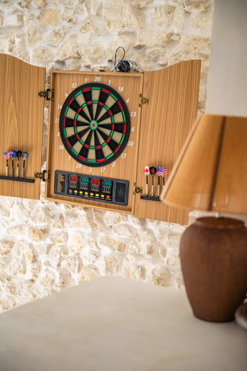 Meuble de fléchettes en bois avec tableau de bord électronique sur mur en pierre à l'hôtel boutique Domaine Mas Lafleur à Châteaurenard