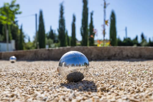 Boule de pétanque sur un terrain de graviers au Domaine Mas Lafleur à Châteaurenard, avec cyprès et jardin en arrière-plan