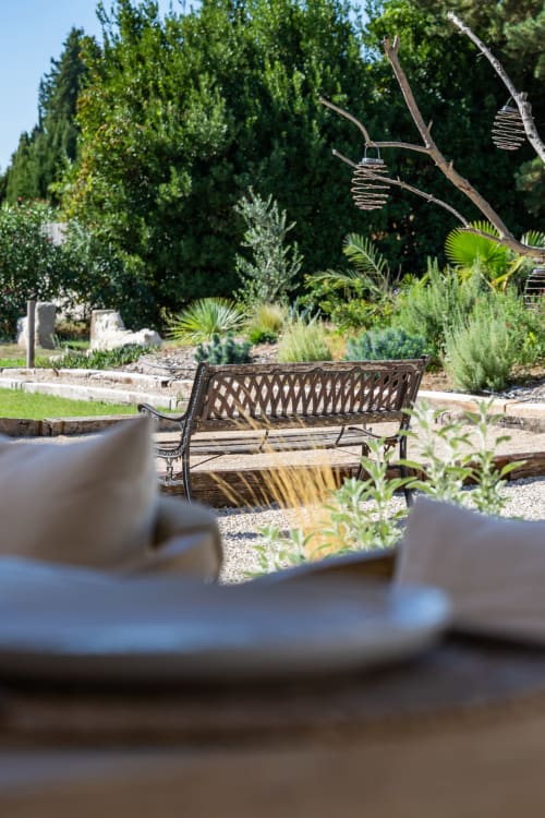 Coin de détente paisible au Domaine Mas Lafleur avec banc métallique, pommes de pin et plantes méditerranéennes sous ciel bleu