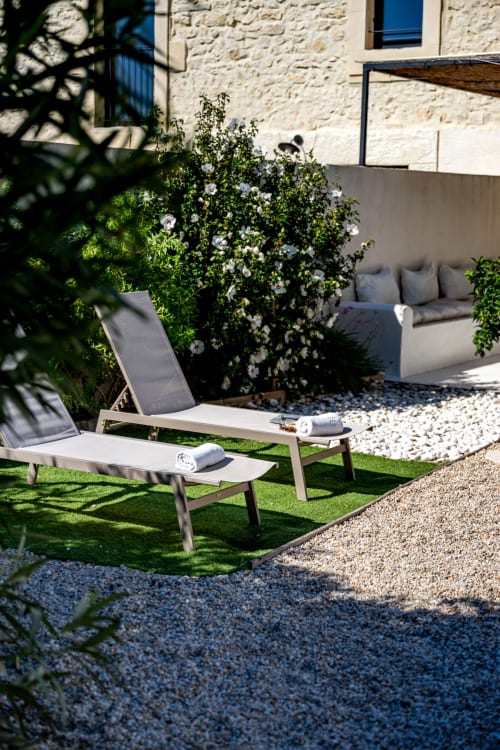 Terrasse ensoleillée du Domaine Mas Lafleur avec transats, vignes à fleurs blanches, murs en pierre et mobilier extérieur moderne