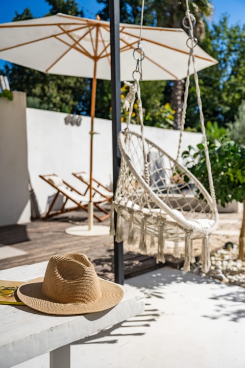 Chapeau de paille sur la table de la terrasse de la villa Domaine Mas Lafleur avec fauteuil suspendu et parasol à Châteaurenard