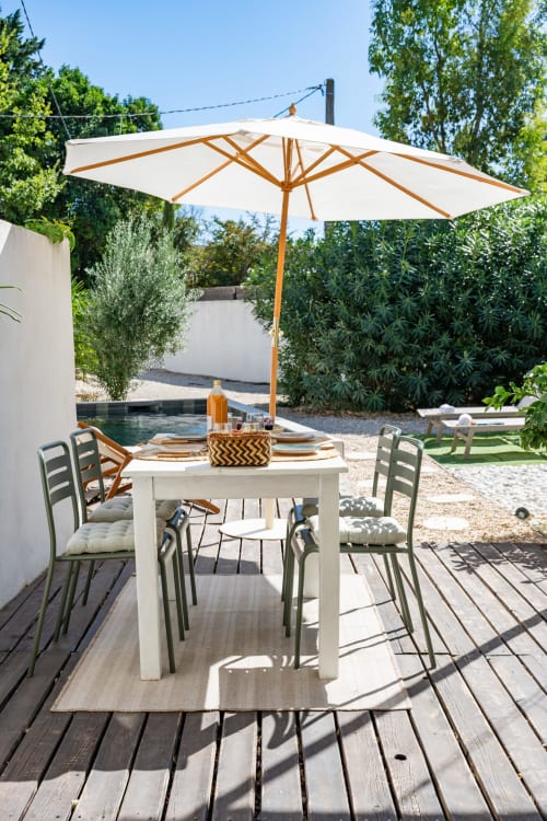 Espace de restauration au bord de la piscine du Domaine Mas Lafleur avec parasol blanc, table et chaises face au jardin à Châteaurenard