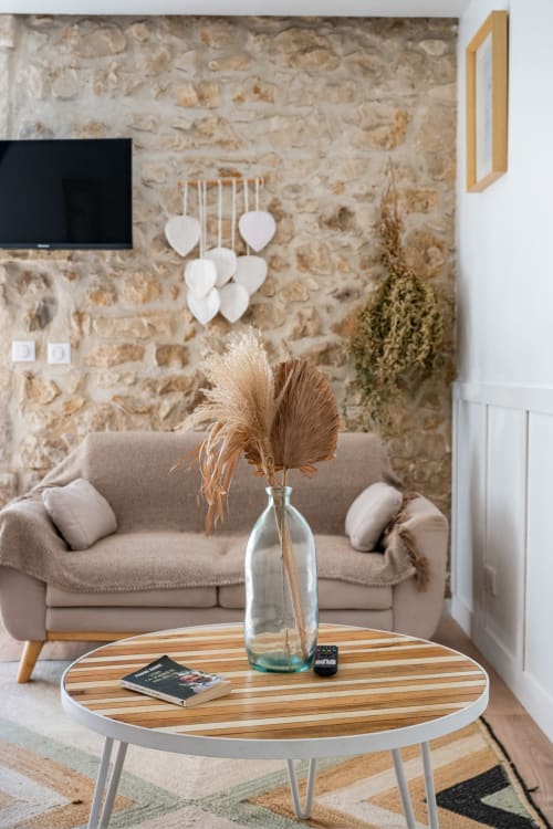 Salon moderne au Domaine Mas Lafleur avec mur en pierre rustique, canapé beige, table en bois et fleurs séchées en vase