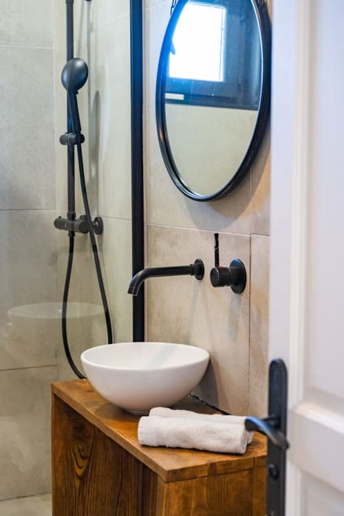 Salle de bain moderne du Domaine Mas Fleur avec vasque blanche, robinetterie noire, miroir ovale et douche à Châteaurenard